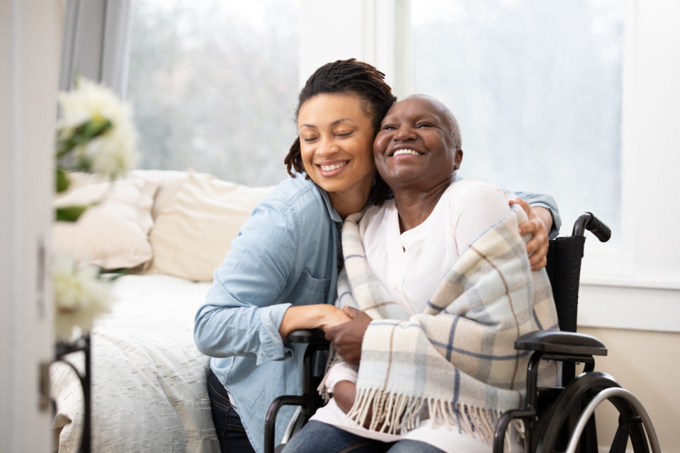 Young woman hugs senior woman in wheelchair