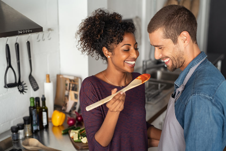 Young couple tasting tomato sauce while cooking in the kitchen.