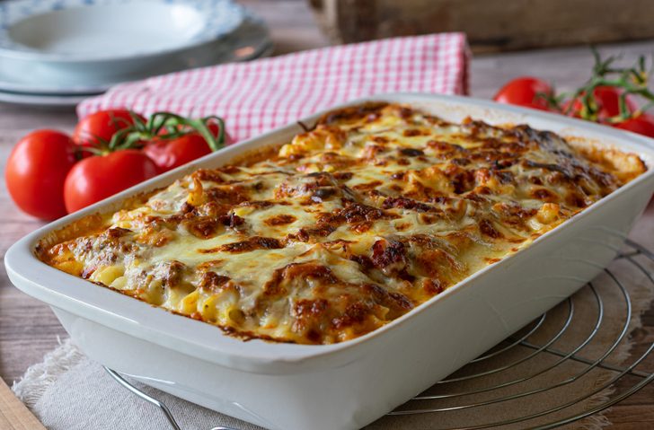 Delicious homemade italian gratin dish with home cooked bolognese sauce and bechamel sauce topped with mozzarella cheese and served in a white baking dish on rustic table background. Closeup view